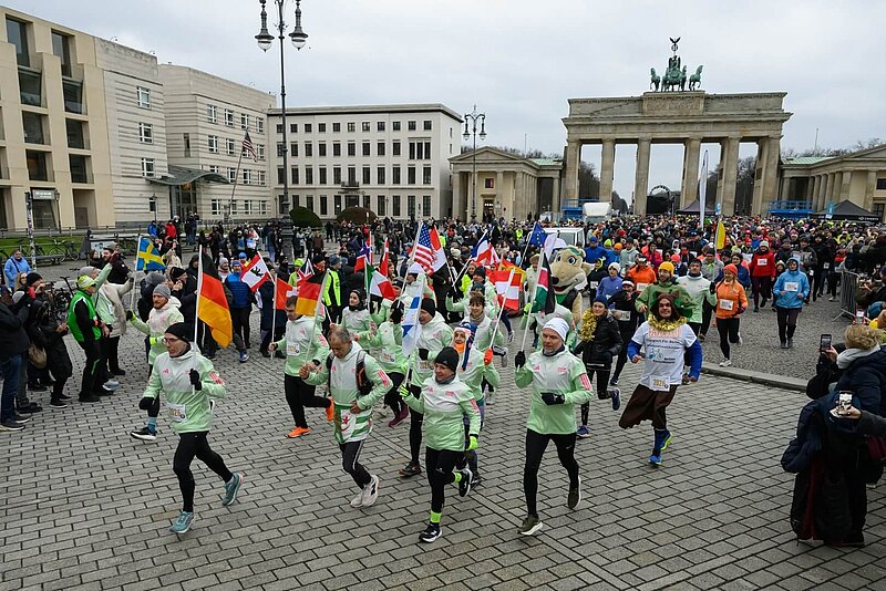 Viele Teilnehmende laufen mit Nationalflaggen auf dem Pariser Platz los.