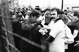 Berliner Neujahrslauf 1990: DDR-Grenzpolizist gibt Teilnehmer:innen des Neujahrslaufes 1990 Passierstempel auf die Startnummer © picture alliance / ZB / Manfred Uhlenhut