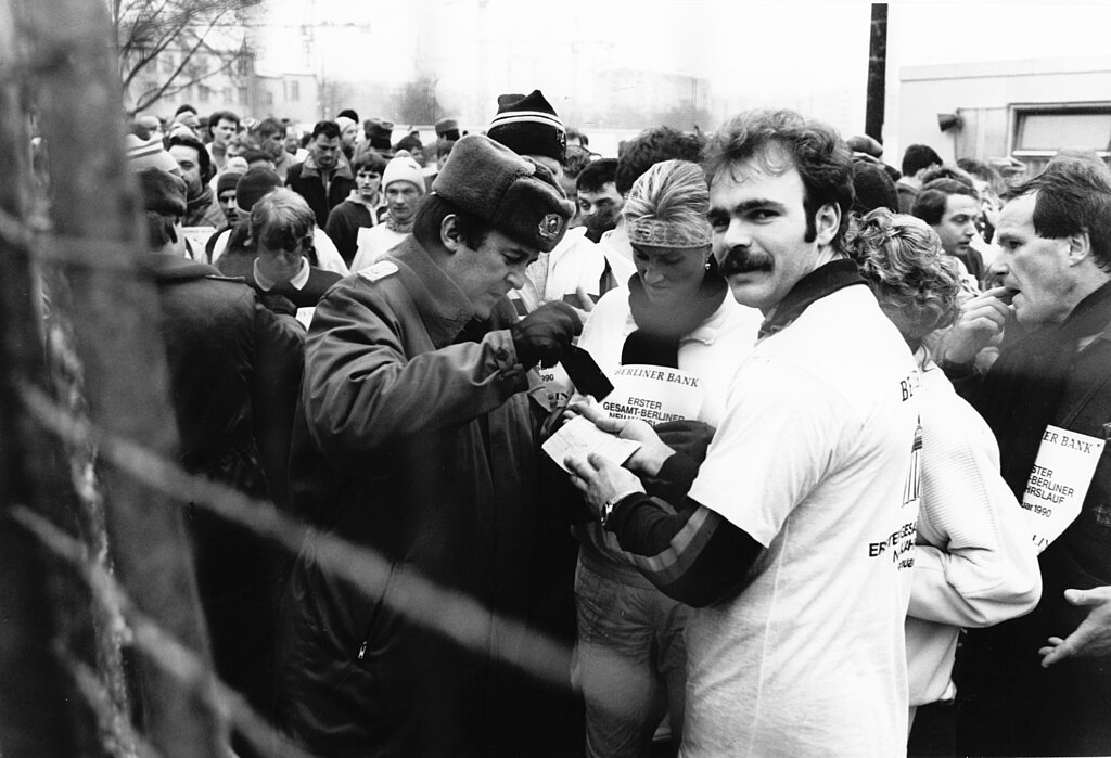 Berliner Neujahrslauf 1990: DDR-Grenzpolizist gibt Teilnehmer:innen des Neujahrslaufes 1990 Passierstempel auf die Startnummer © picture alliance / ZB / Manfred Uhlenhut