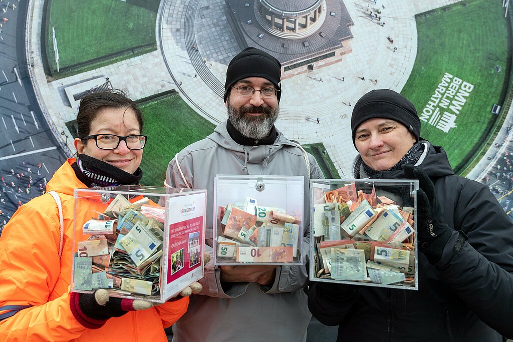 Berliner Neujahrslauf 2020: Drei Kassetten mit Geldspenden werden von 3 Volunteers in die Kamera gehalten © SCC EVENTS / camera4