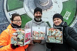 Berlin New Year's Run 2020: Three cassettes with money donations are held up to the camera by 3 volunteers © SCC EVENTS / camera4