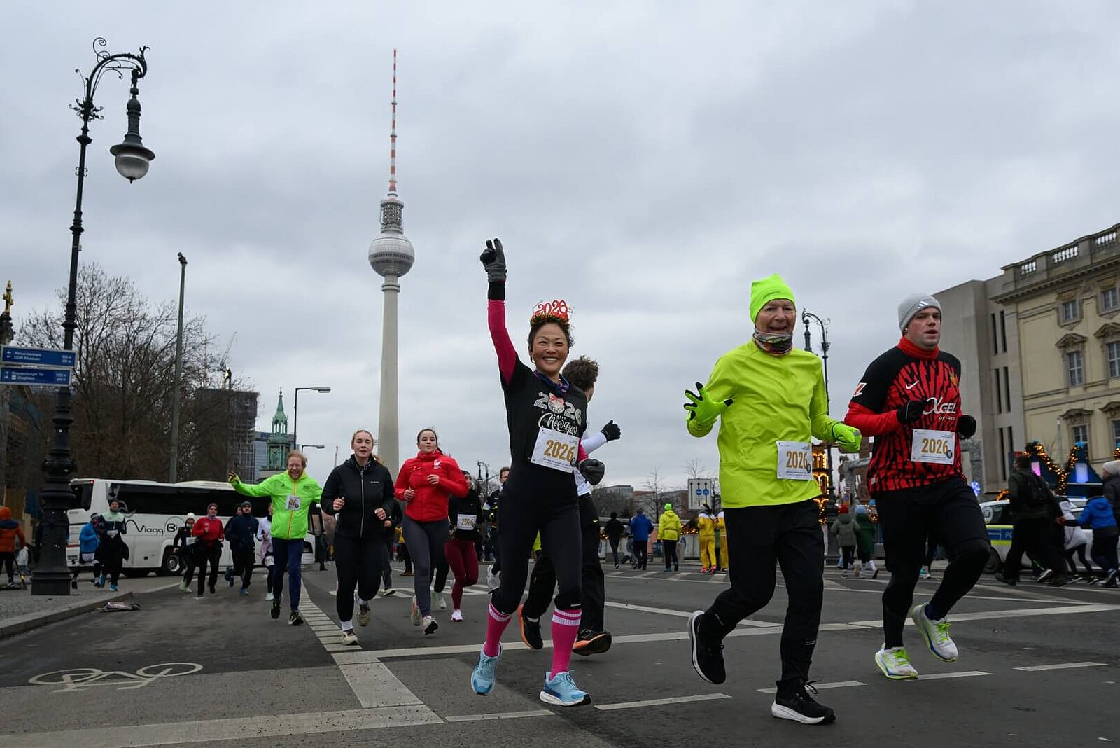 Teilnehmende winken in die Kamera. Im Hintergrund der Fernsehturm.