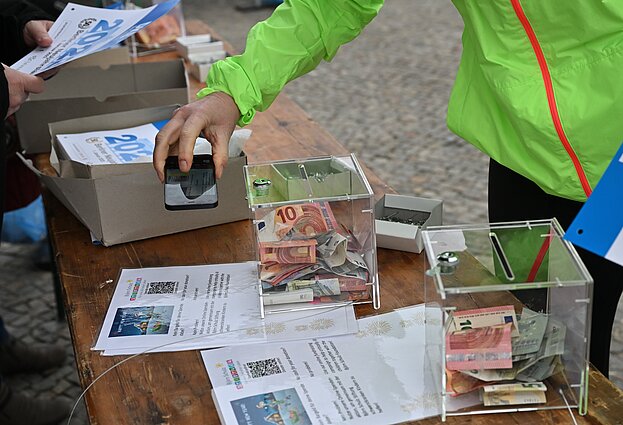 Berliner Neujahrslauf 2023: Läufer:in spendet bei der Ausgabe der Startnummern © SCC EVENTS / Petko Beier